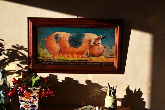 a large painting of a pig in Victorian style with a dark wooden frame hangs on a pink wall