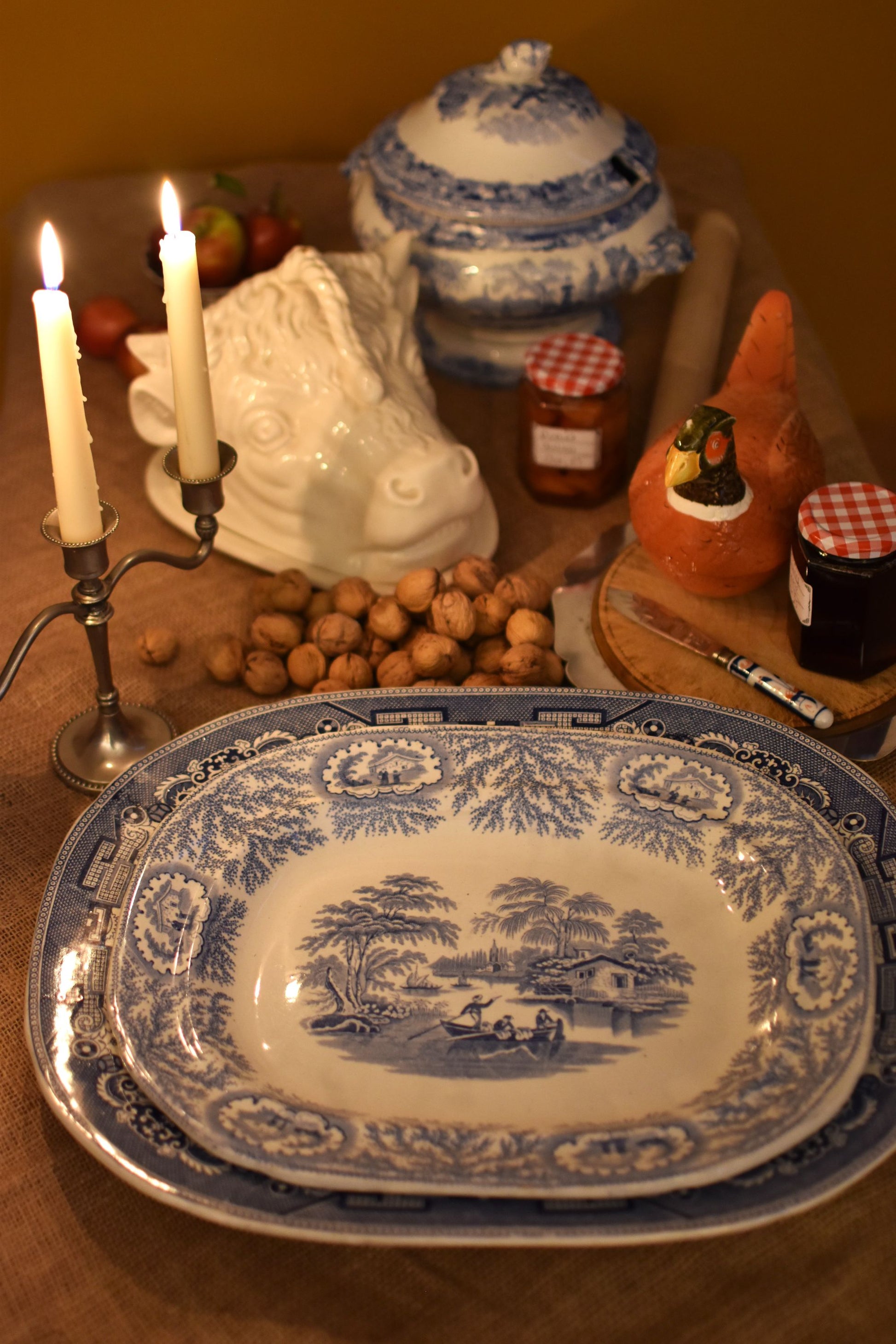 Decorative blue and white platter on a table with candles, fruit, and other items.