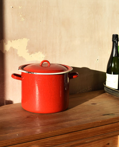 a big red pot or saucepan sits on a wooden worktop against a pink background