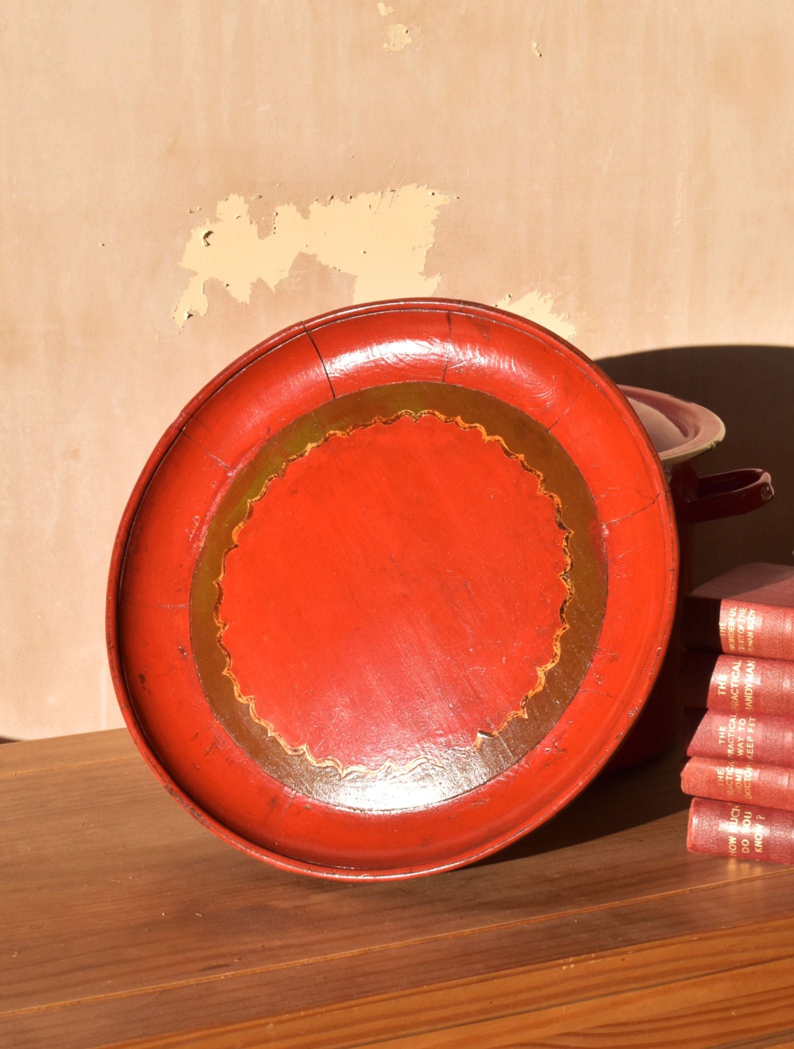 Large red plate made of wood leans against a pink wall, on top of a wooden table
