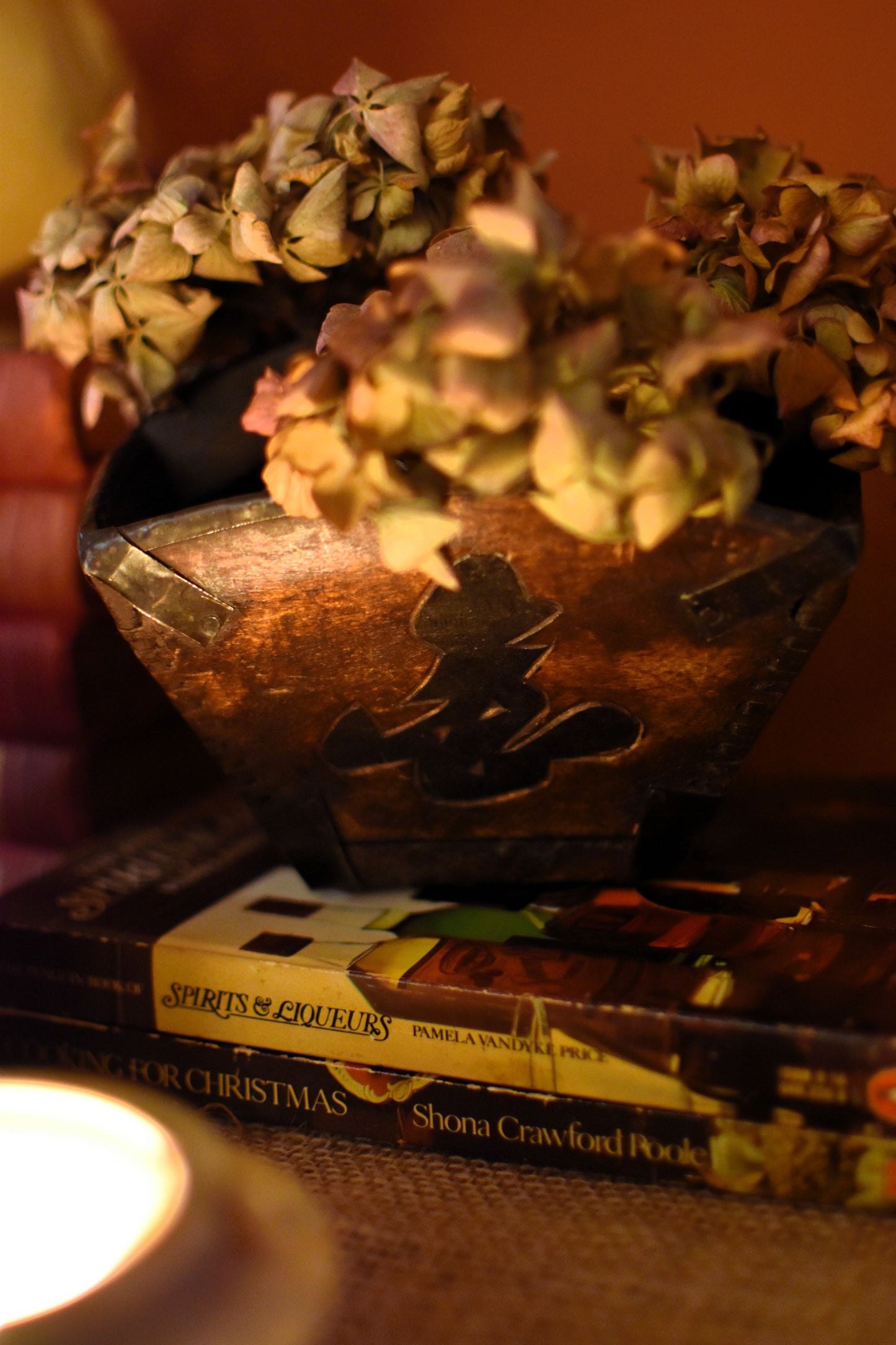Decorative bowl with dried flowers on top of books, with a warm glow.