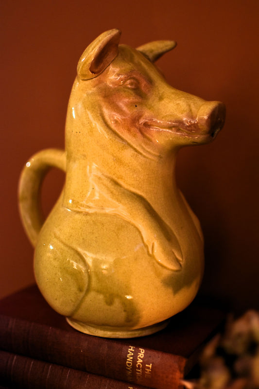 Yellow ceramic pig-shaped pitcher on a dark surface with a brown background