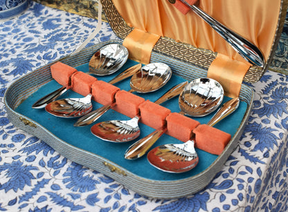 Set of silver spoons in a decorative tray on a patterned tablecloth