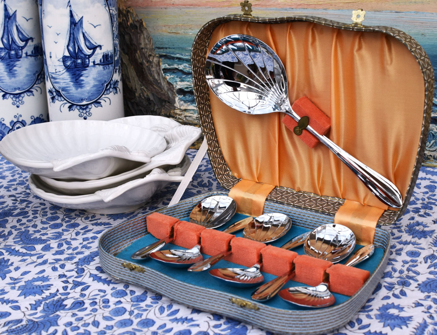 Set of silver spoons in a decorative case on a blue and white patterned tablecloth.