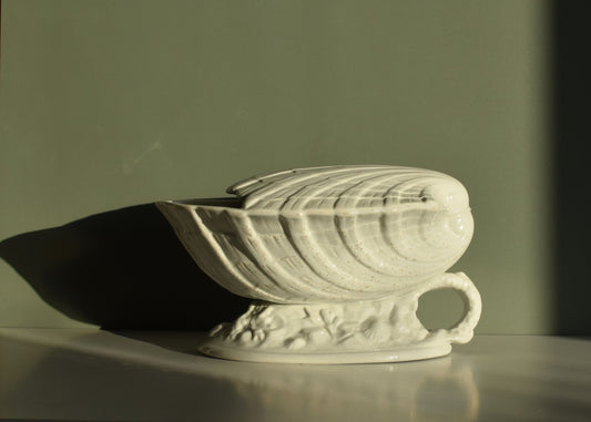 White ceramic spoon warmer with handle on a reflective surface against a dark background
