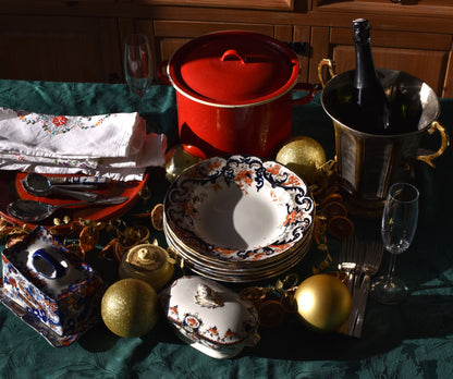 a table is set with plates,dishes, a big red pot and christmas baubles