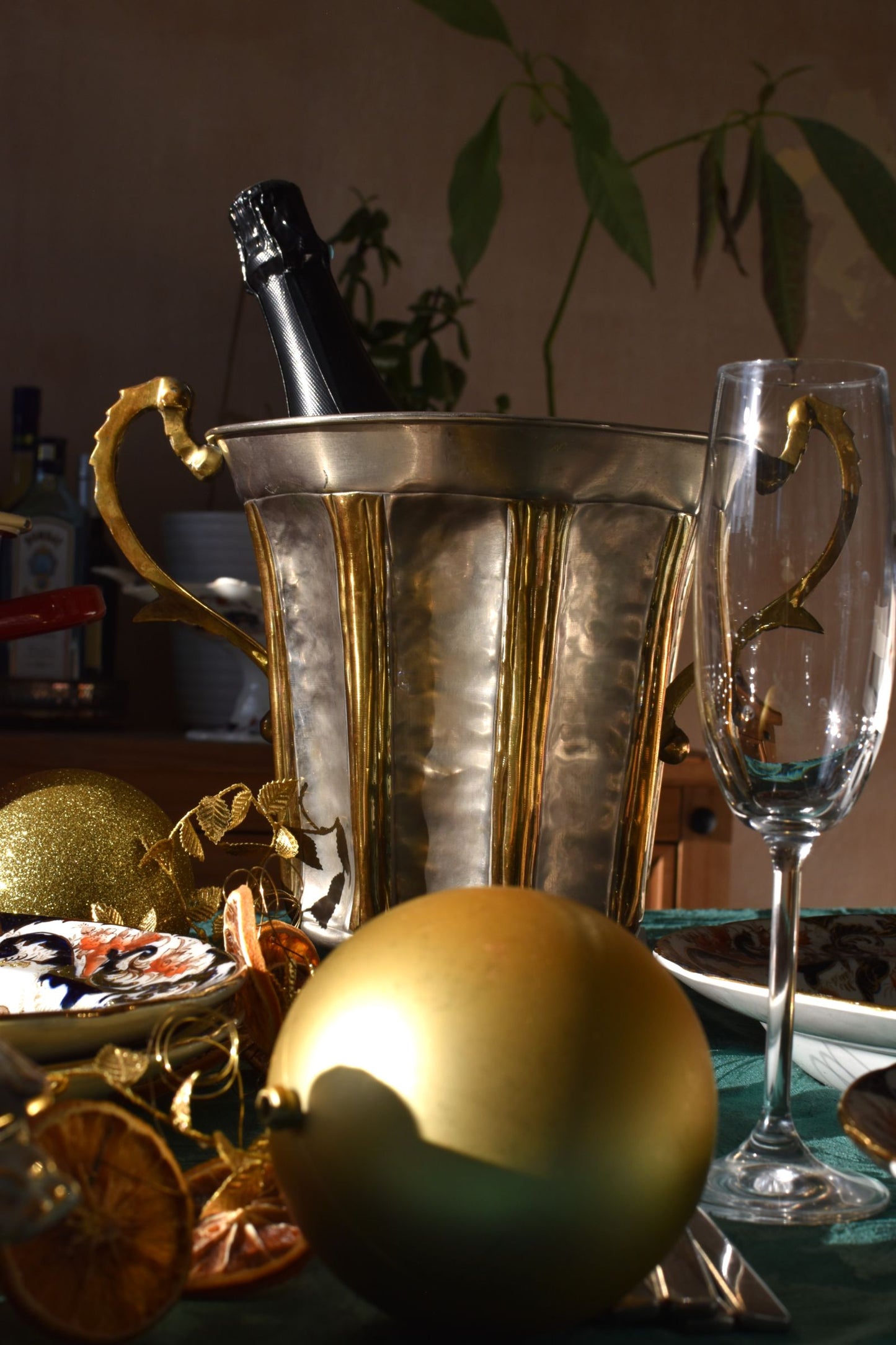 a silver and gold ice bucket with a bottle of champagne inside is on a table full of glasses, plates and baubles