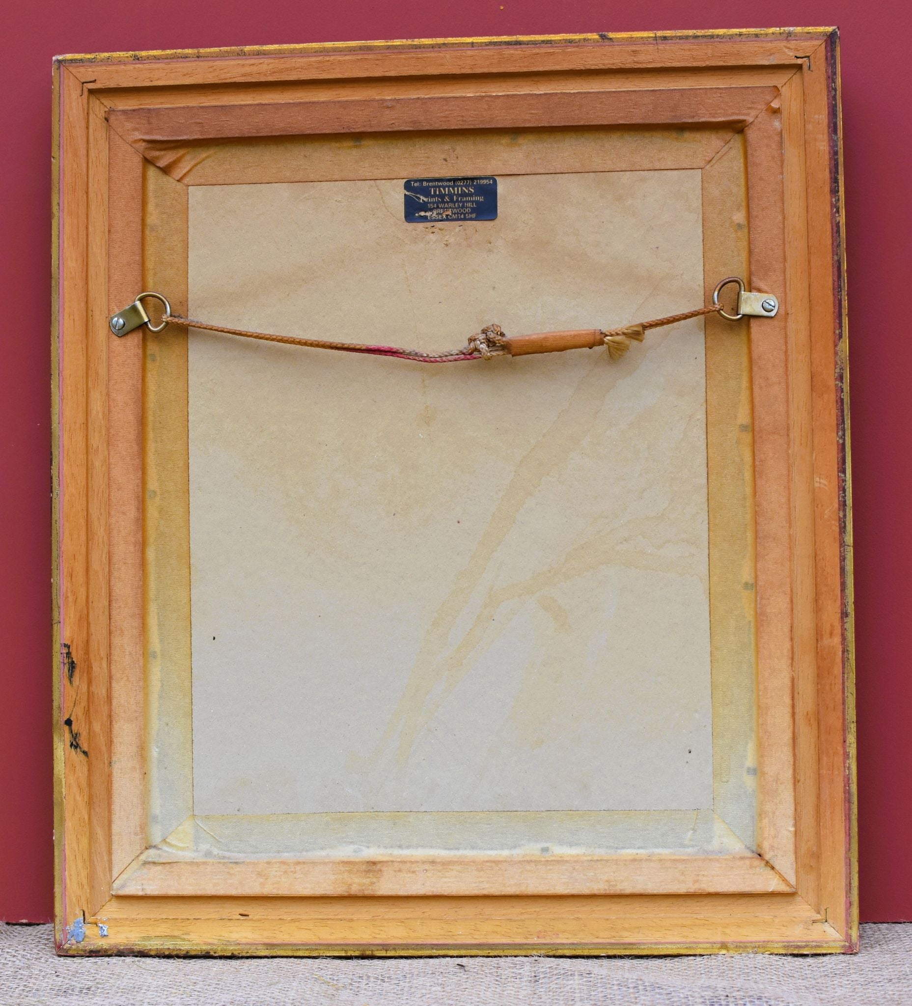 Back of a painting with a wooden frame and visible hardware on a red background