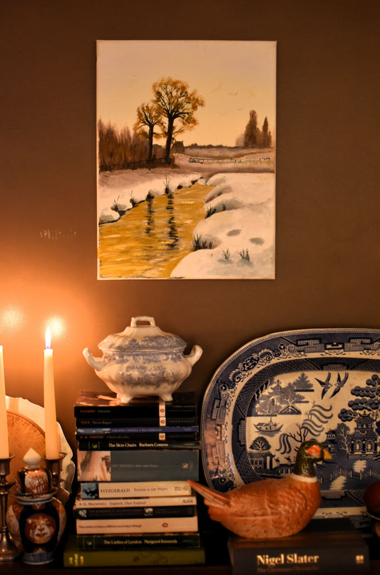 A shelf of books and decorative china with a painting above showing a wintery river and trees
