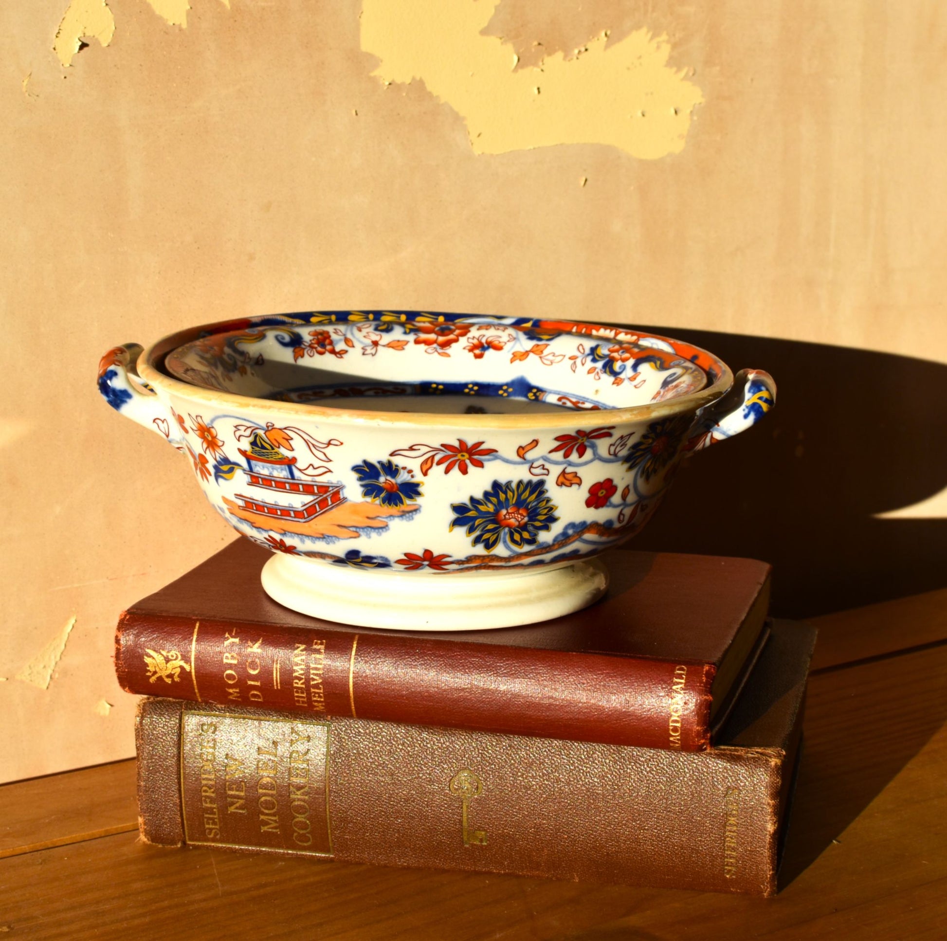 Decorative bowl with floral patterns on top of vintage books against a wooden background