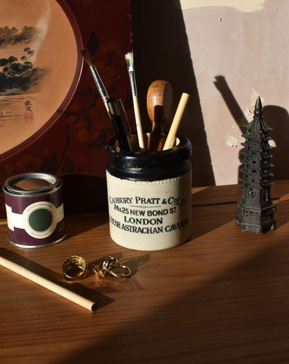 Ceramic container with brushes and other items on a wooden surface with a painting in the background