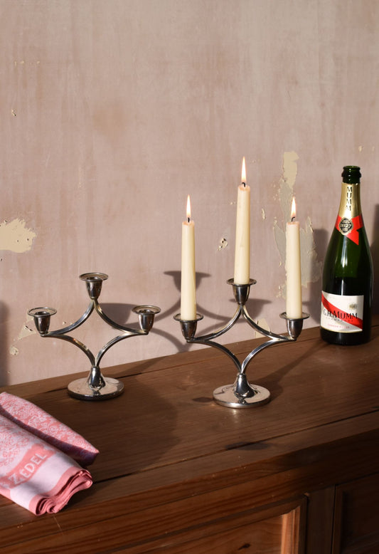 two silver candelabras are on a wooden table with a bottle of champagne