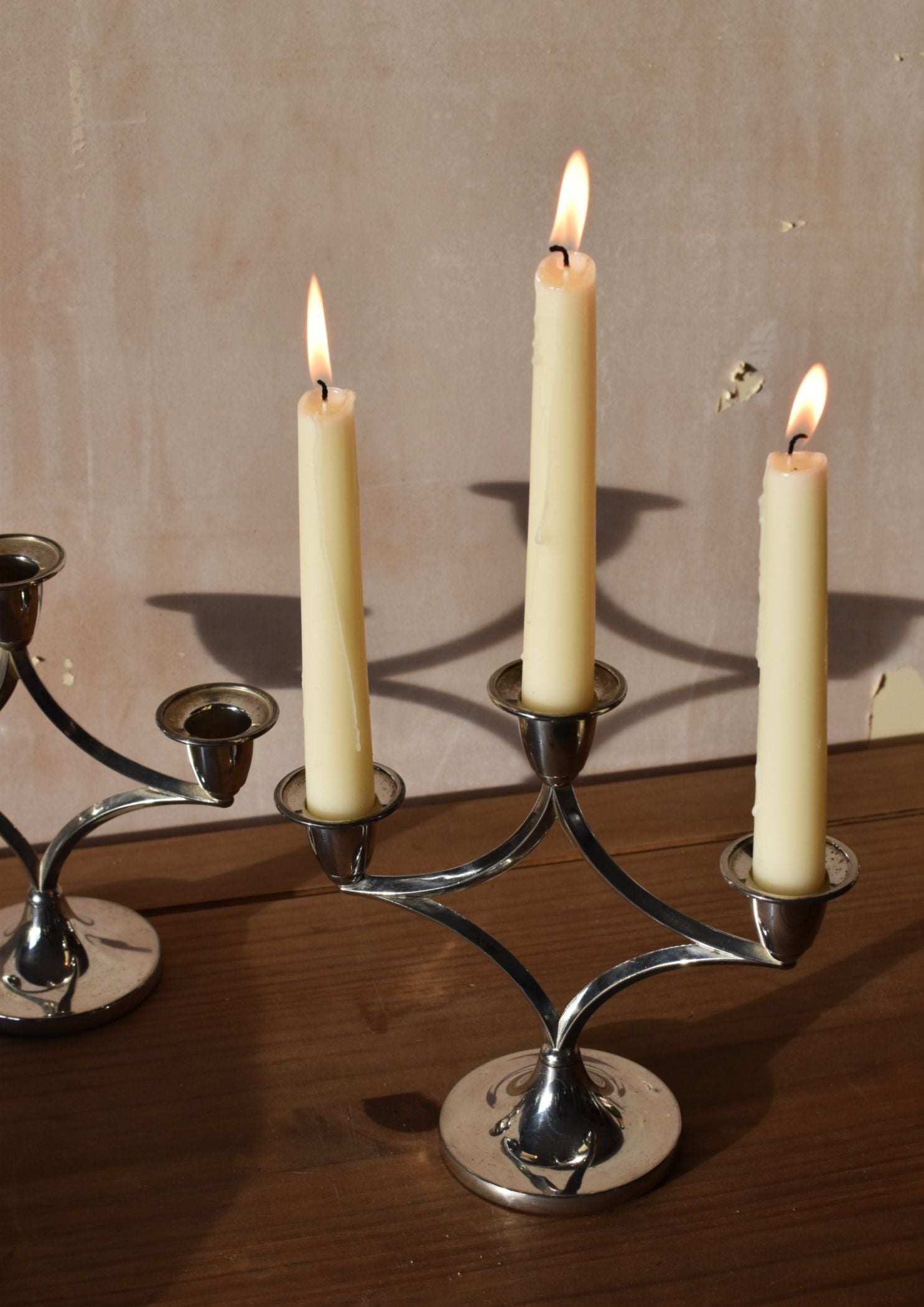 a silver candelabra on a wooden table with three tall white candles lit