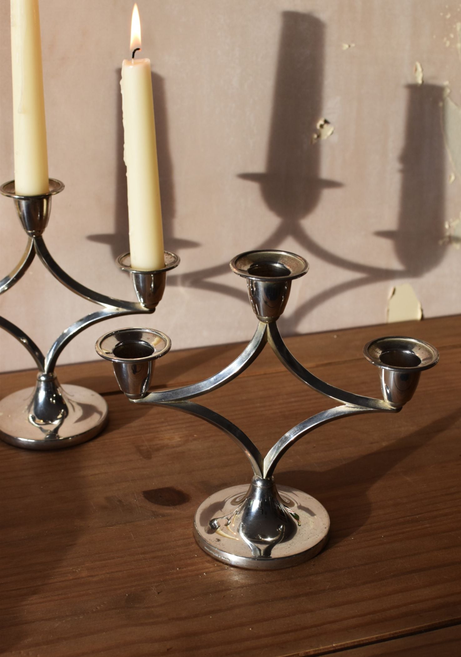 a silver candelabra on a wooden table with no candles, in front of another candelaba with candles