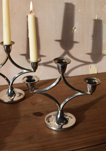 a silver candelabra on a wooden table with no candles, in front of another candelaba with candles