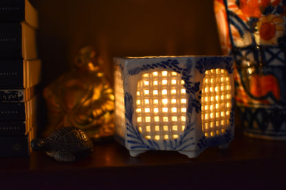 Decorative lamp with a woven design on a shelf with books and a colorful item in the background.