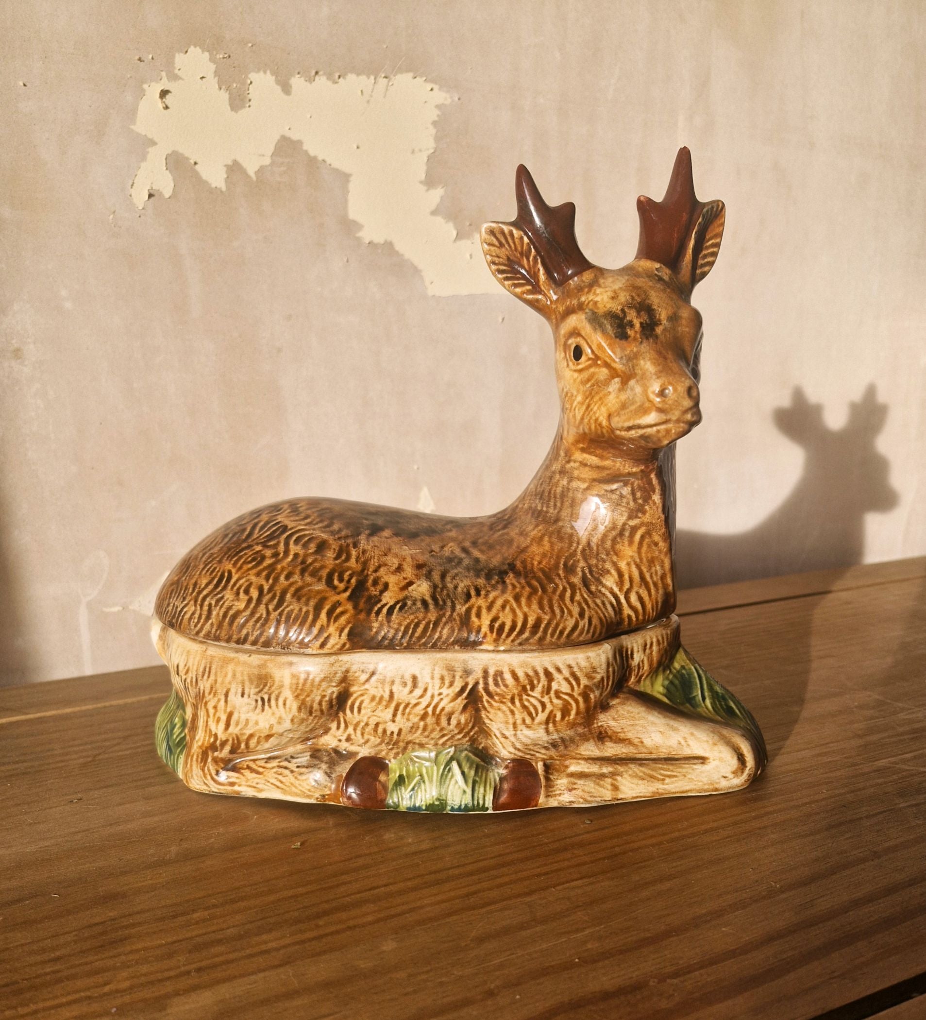 a covered tureen in the shape of a stag with antlers against a brown wall