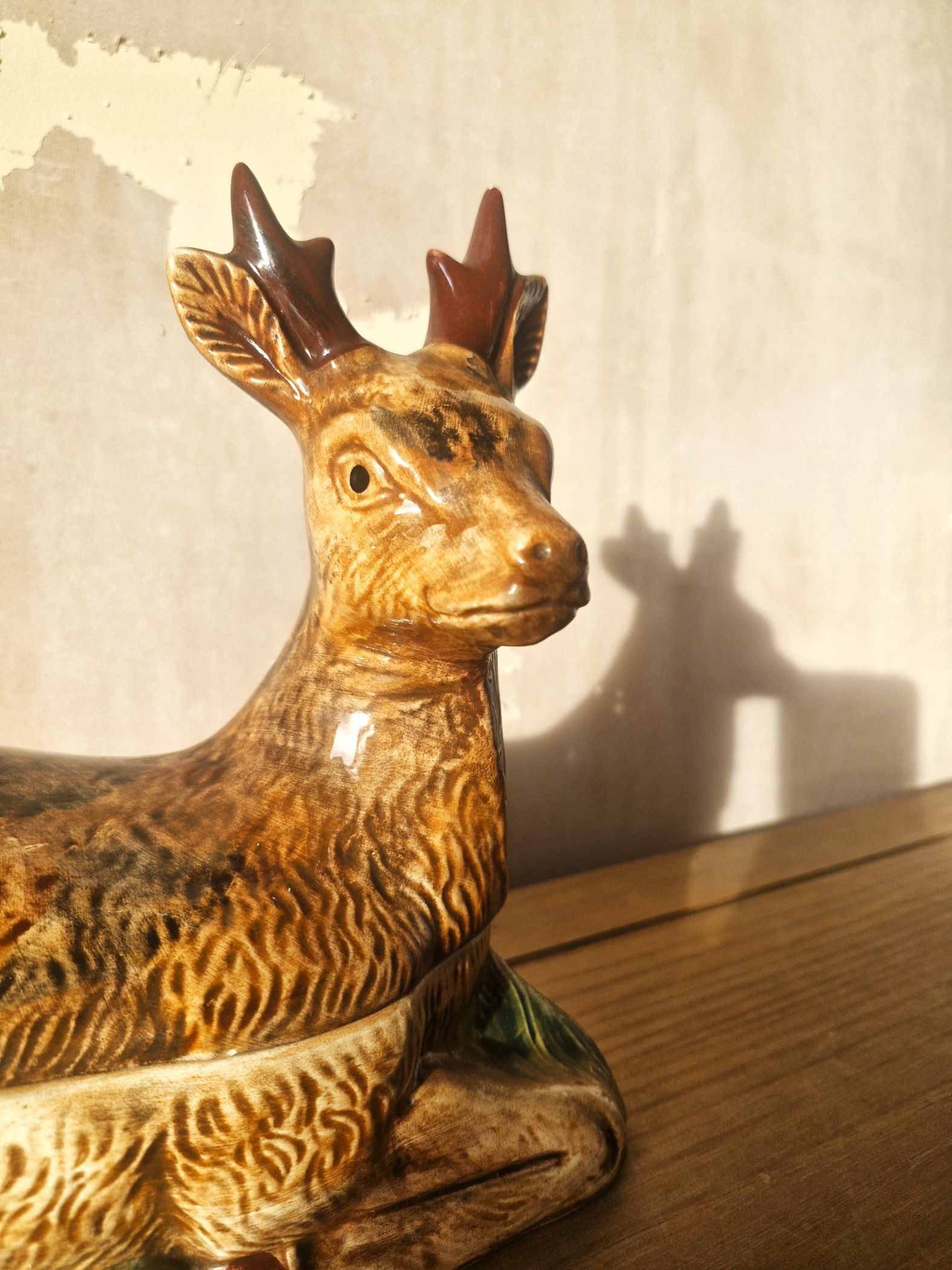 Ceramic deer figurine on a wooden surface with a neutral background
