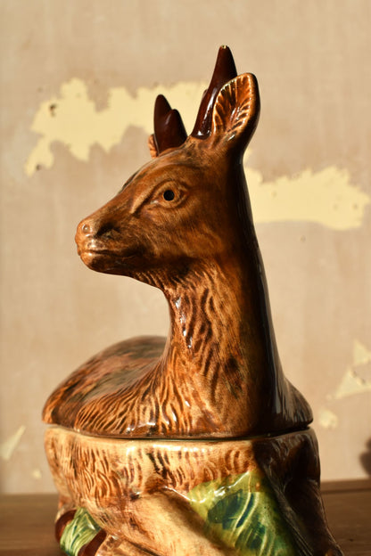Decorative ceramic deer terrine lid on a wooden surface with a textured wall background.