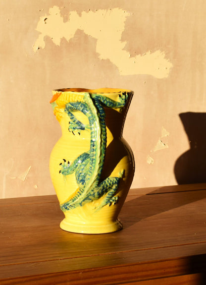 Yellow vase with green dragon design on a wooden surface against a beige wall.