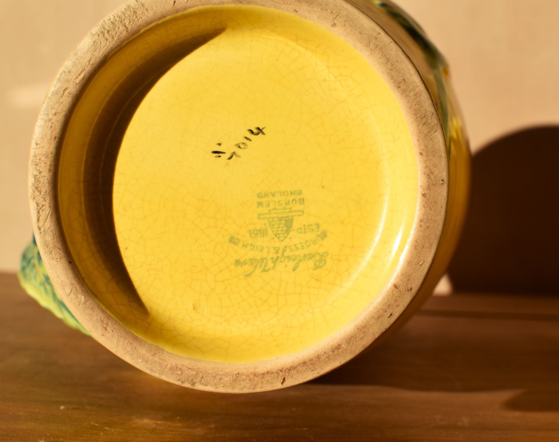 Close-up of a ceramic vase with a visible brand name on a wooden surface.