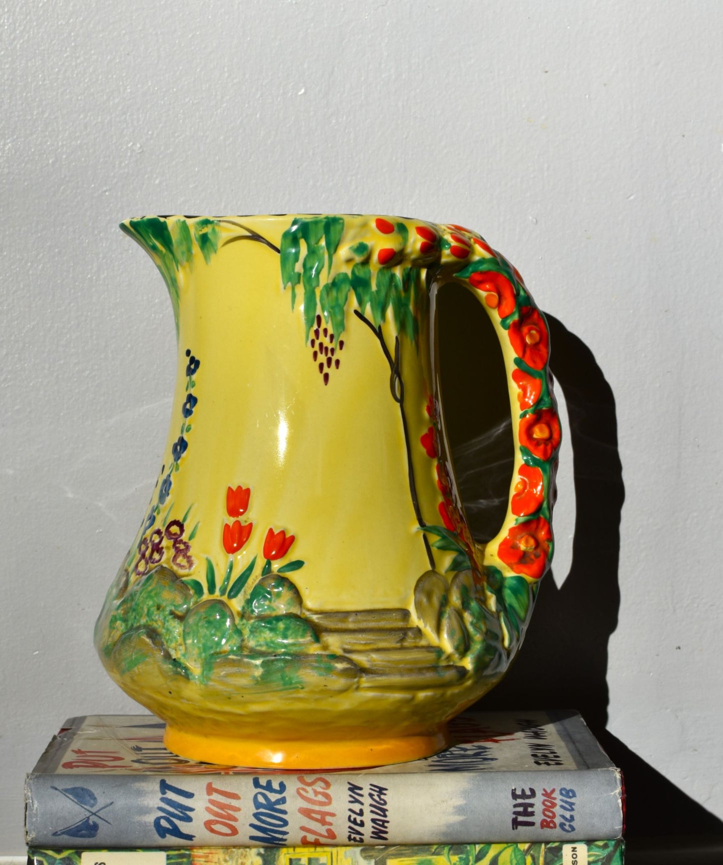 Colorful ceramic pitcher with floral design on a stack of books against a plain background