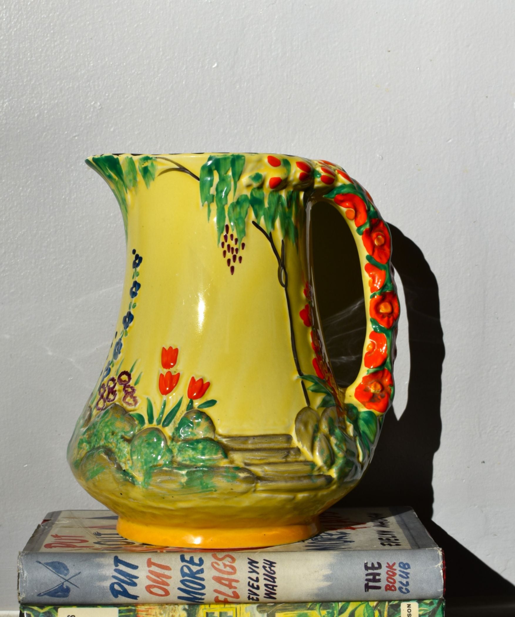 Colorful ceramic pitcher with floral design on a stack of books against a plain background