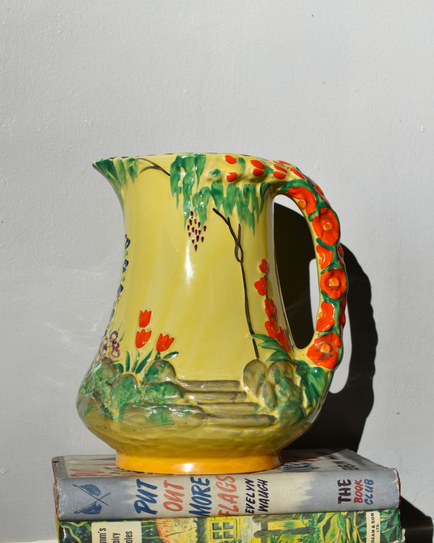 Colorful ceramic pitcher with floral design on a stack of books against a plain background
