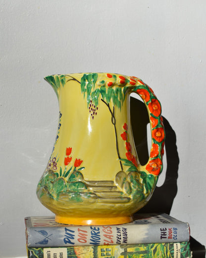 Colorful ceramic pitcher with floral design on a stack of books against a plain background