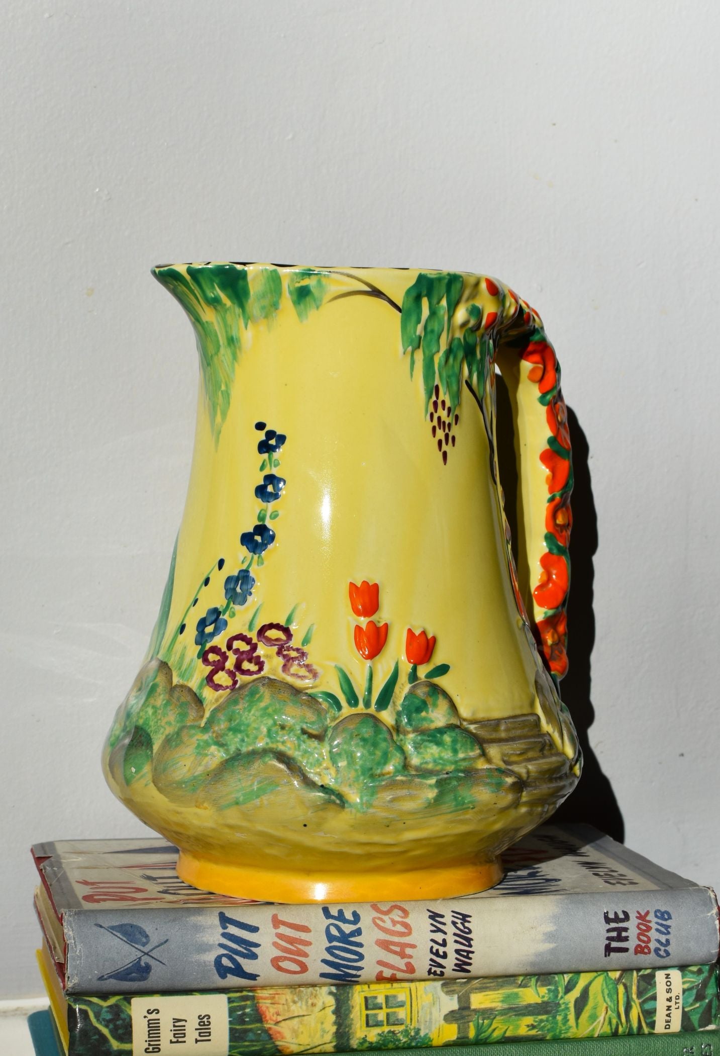 Decorative pitcher with floral design on a stack of books against a plain background