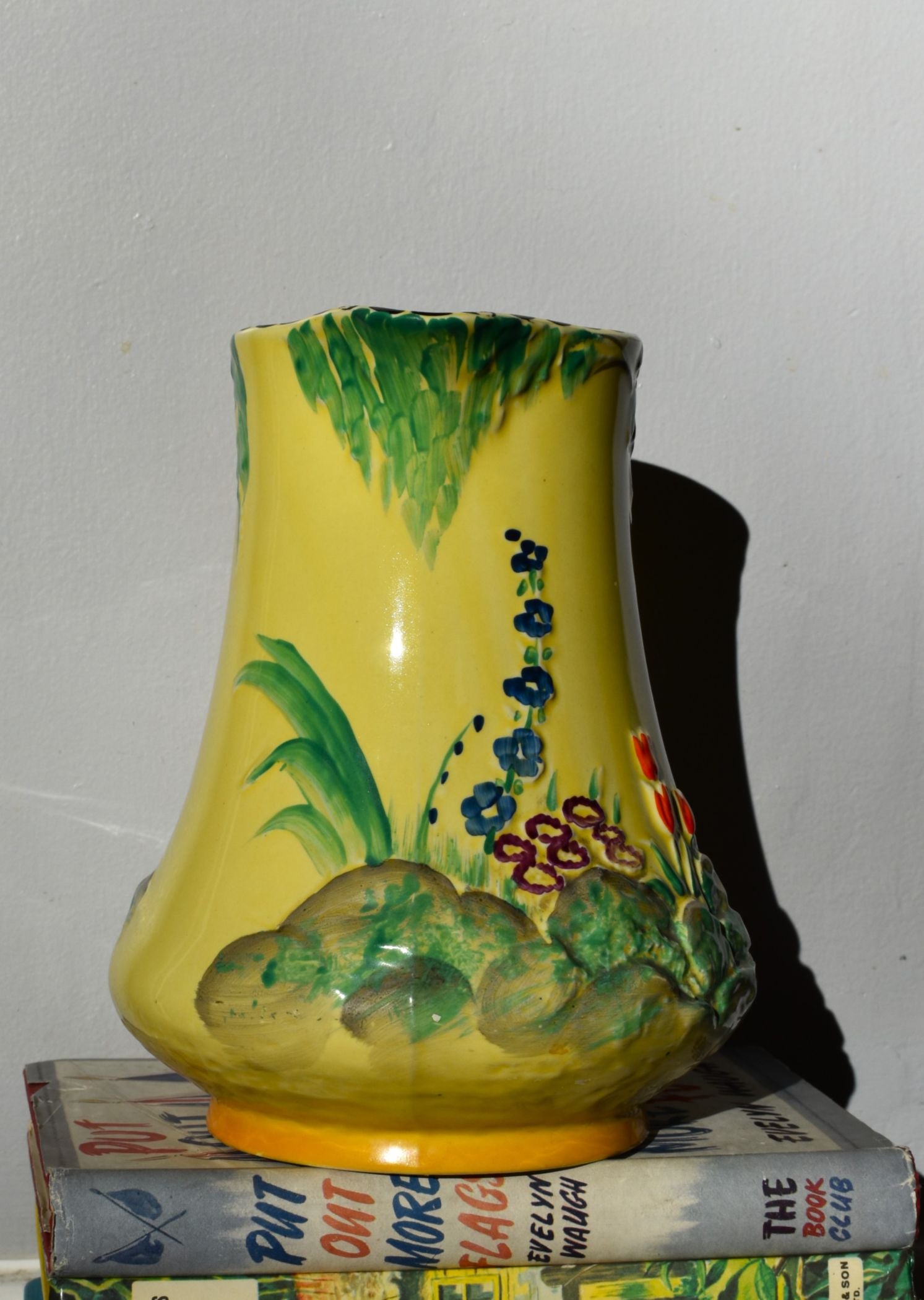 Yellow vase with floral design on a stack of books against a white wall