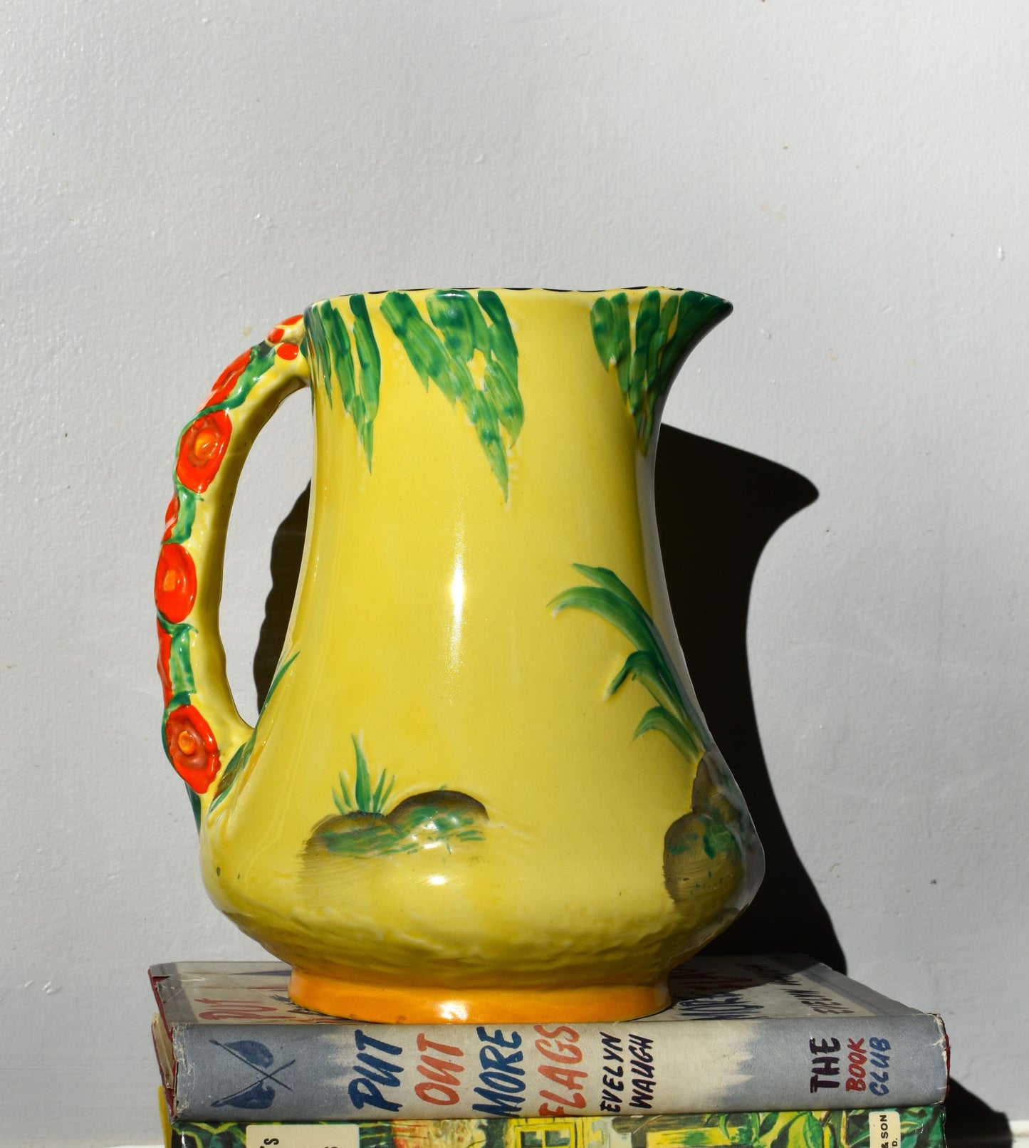 Yellow ceramic pitcher with green leaves and red flowers on a white background