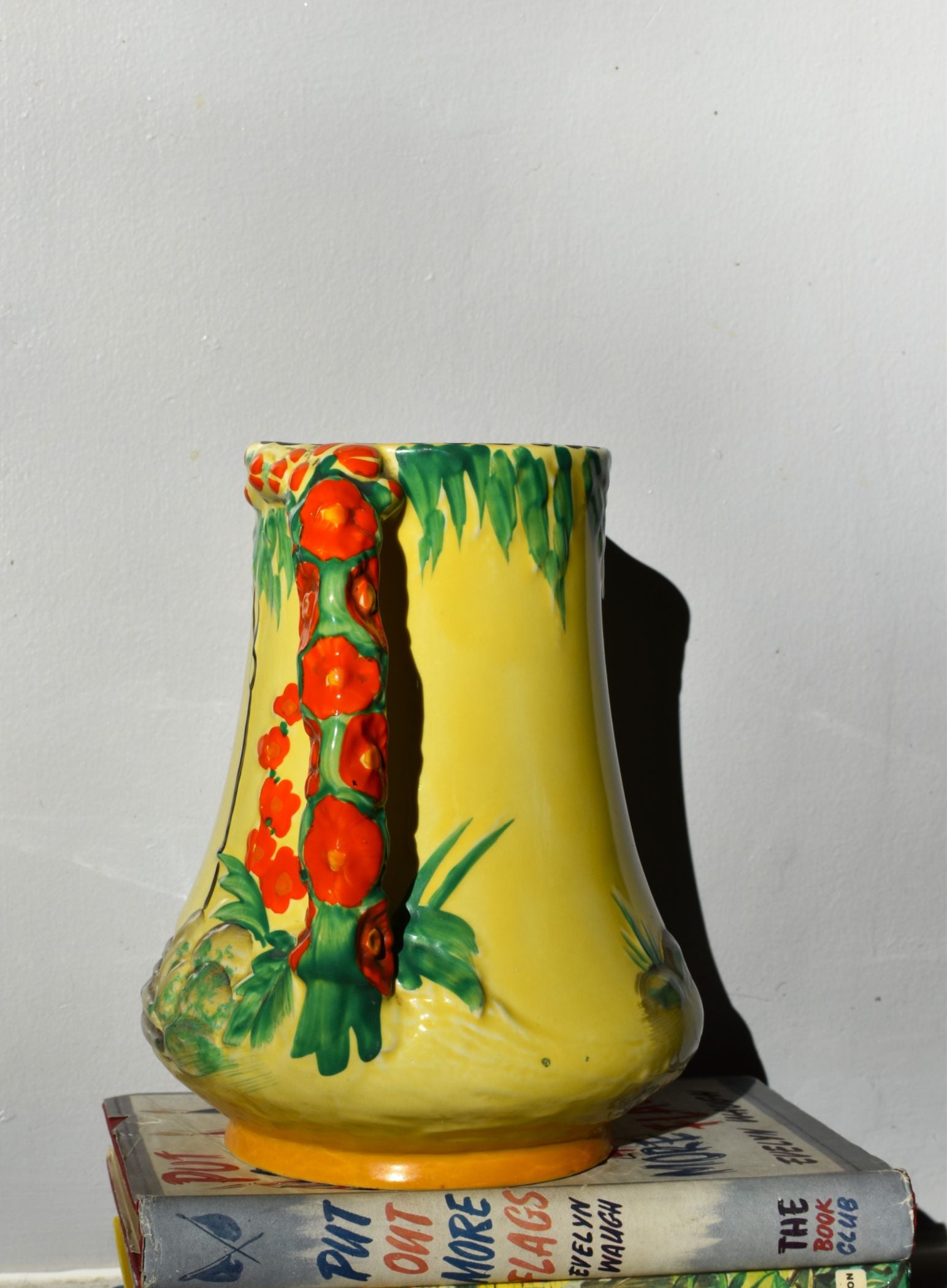 Decorative vase with floral design on a stack of books against a plain background
