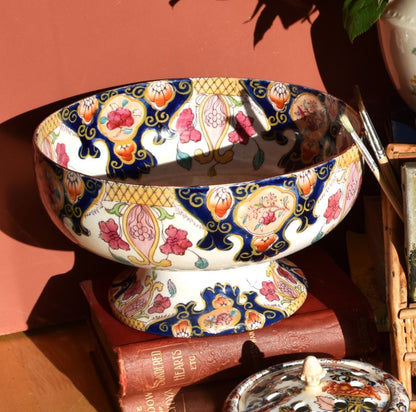 Decorative items including a floral  bowl and books on a wooden surface with a pinkish-brown background.