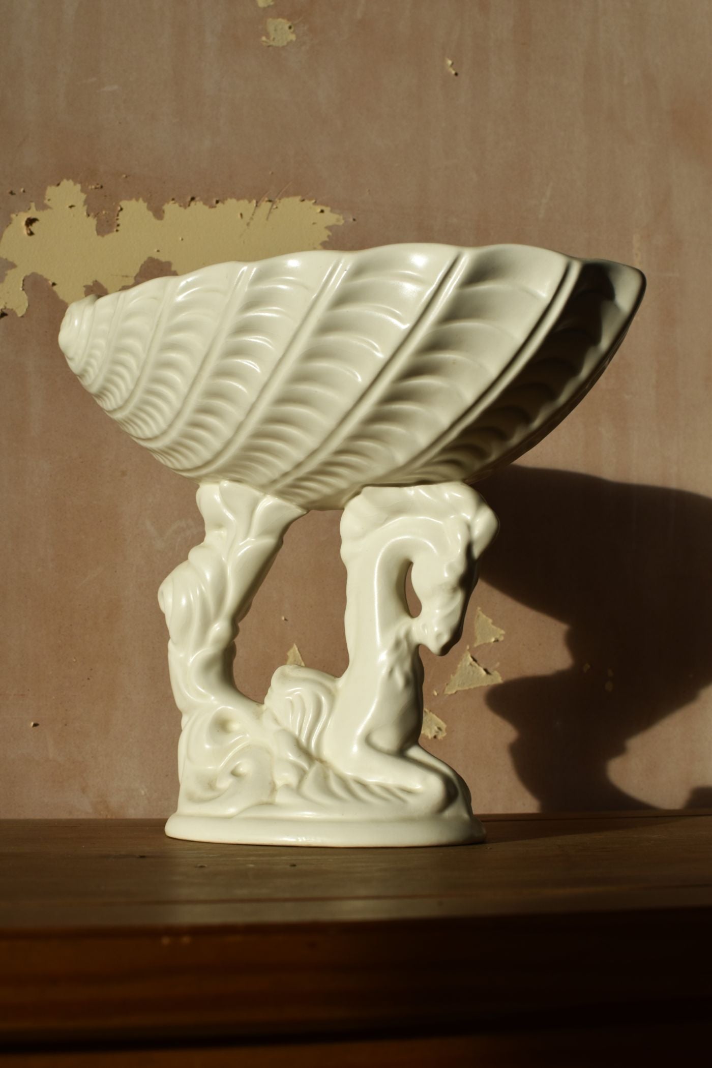 Decorative ceramic shell with seahorse figures on a wooden surface against a brown wall.