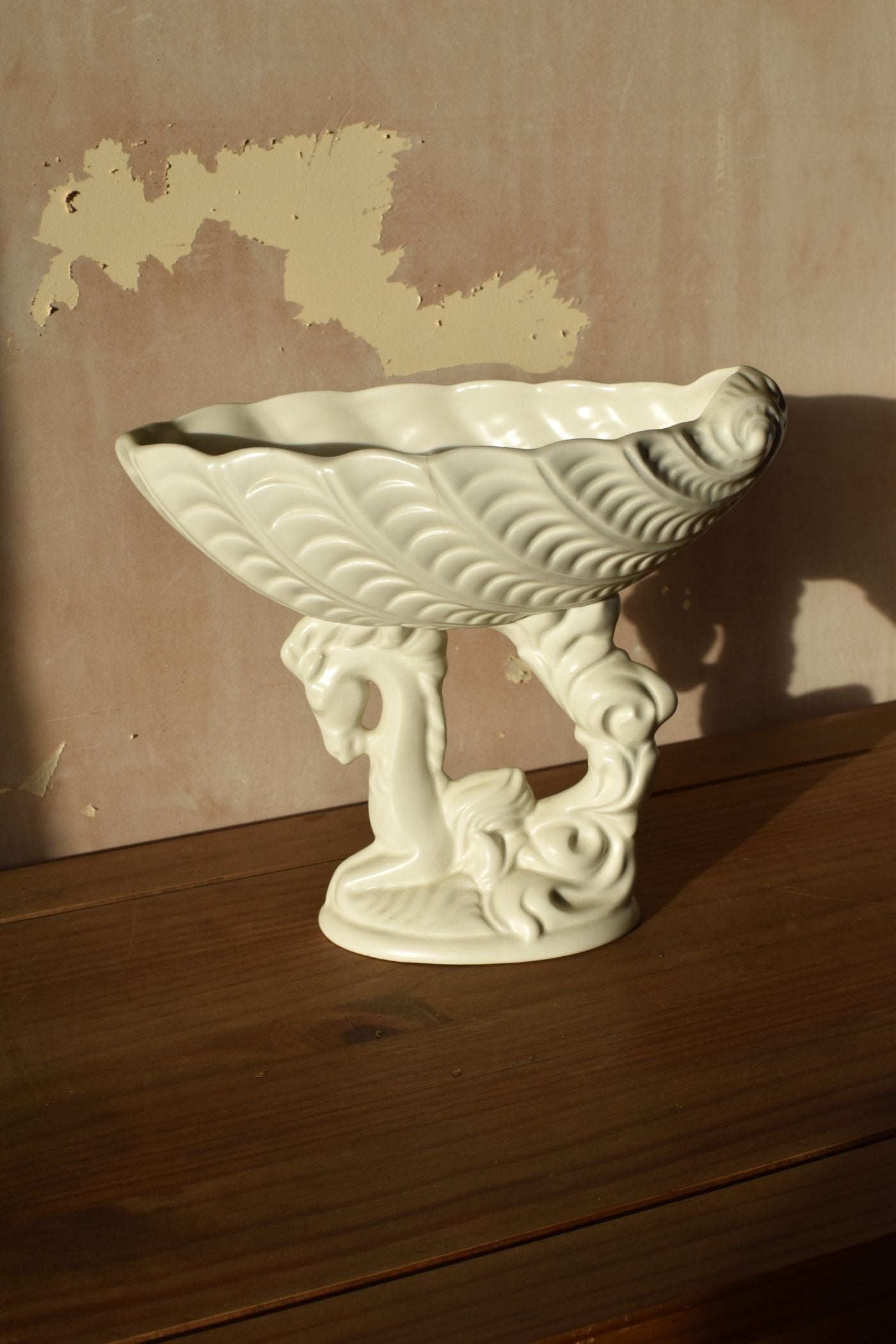 a white ceramic vase in the shape of a shell on top of a seahorse on a wooden surface