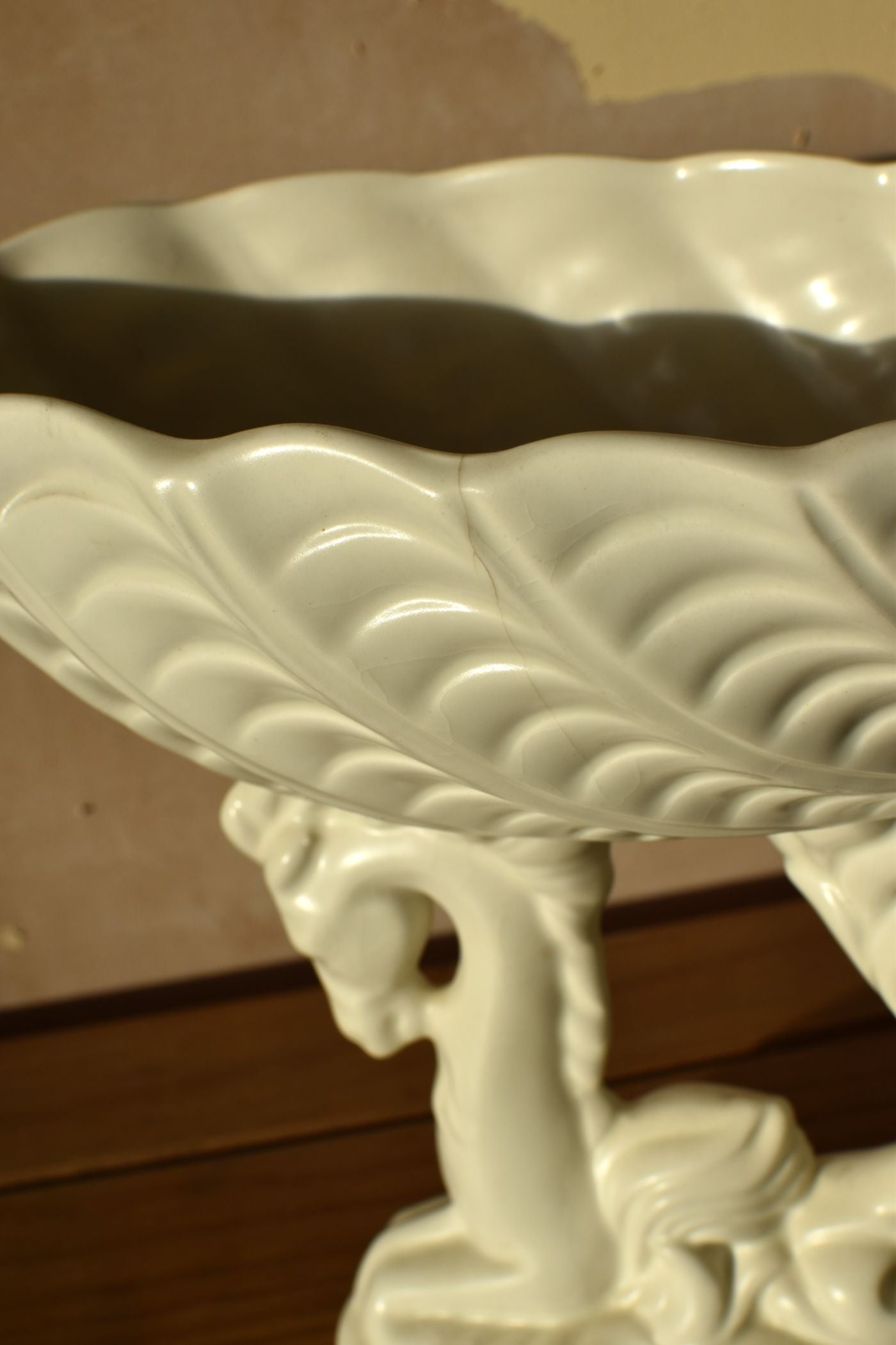 a white ceramic vase in the shape of a shell on top of a seahorse on a wooden surface