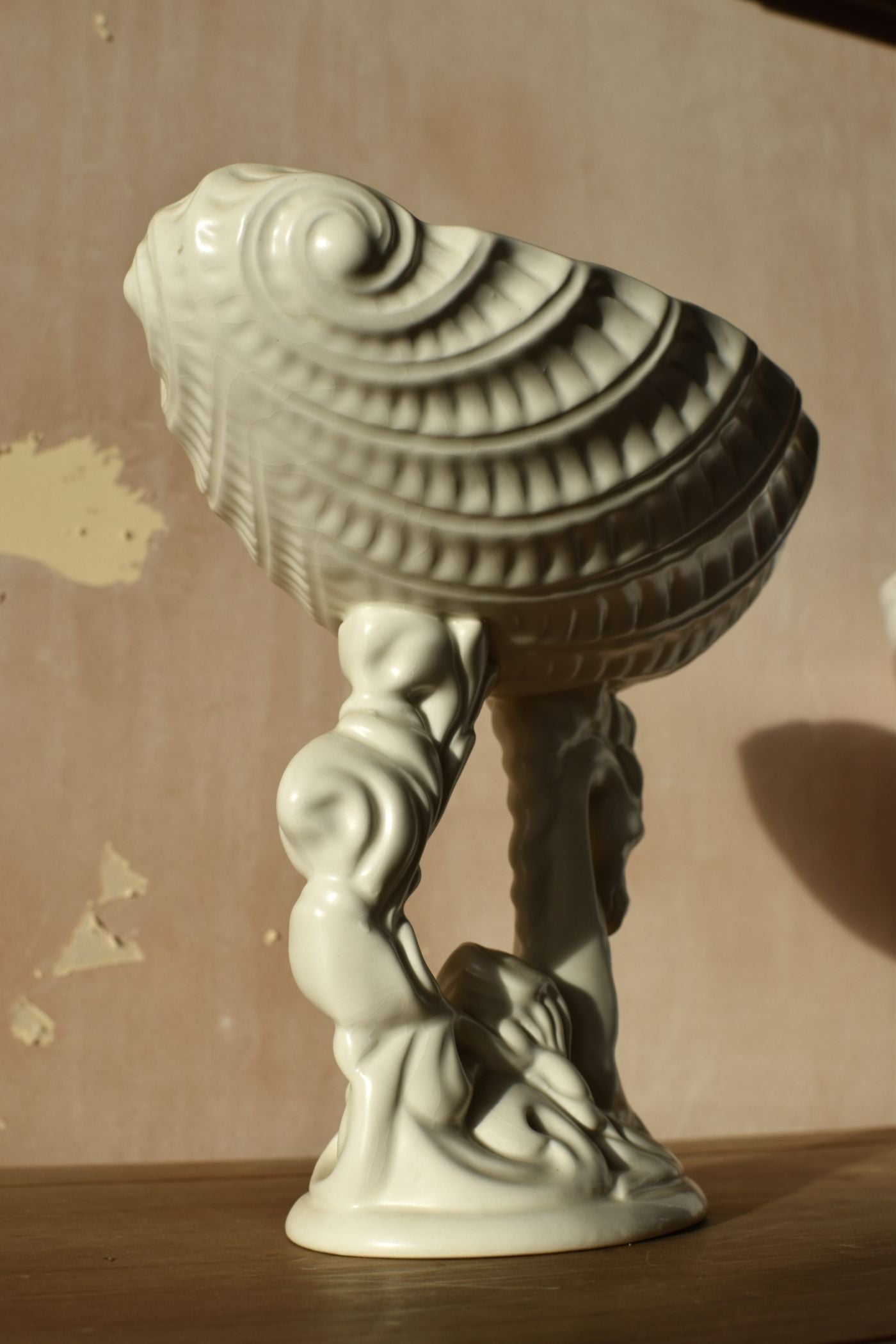 Decorative white ceramic sculpture of a figure holding a shell against a plain background