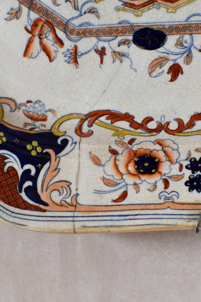 Close-up of a decorative plate with floral and paisley patterns. The plate is cracked