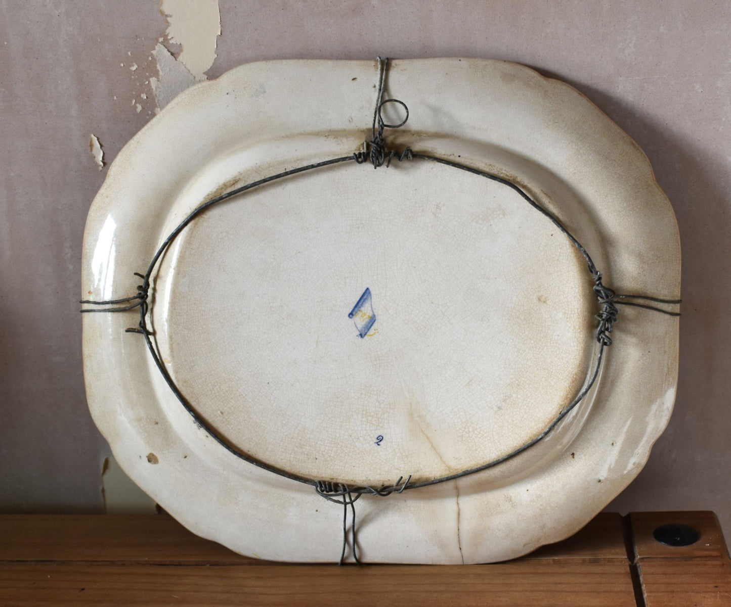 Vintage oval ceramic platter with hanging wire on a wooden surface and beige wall background