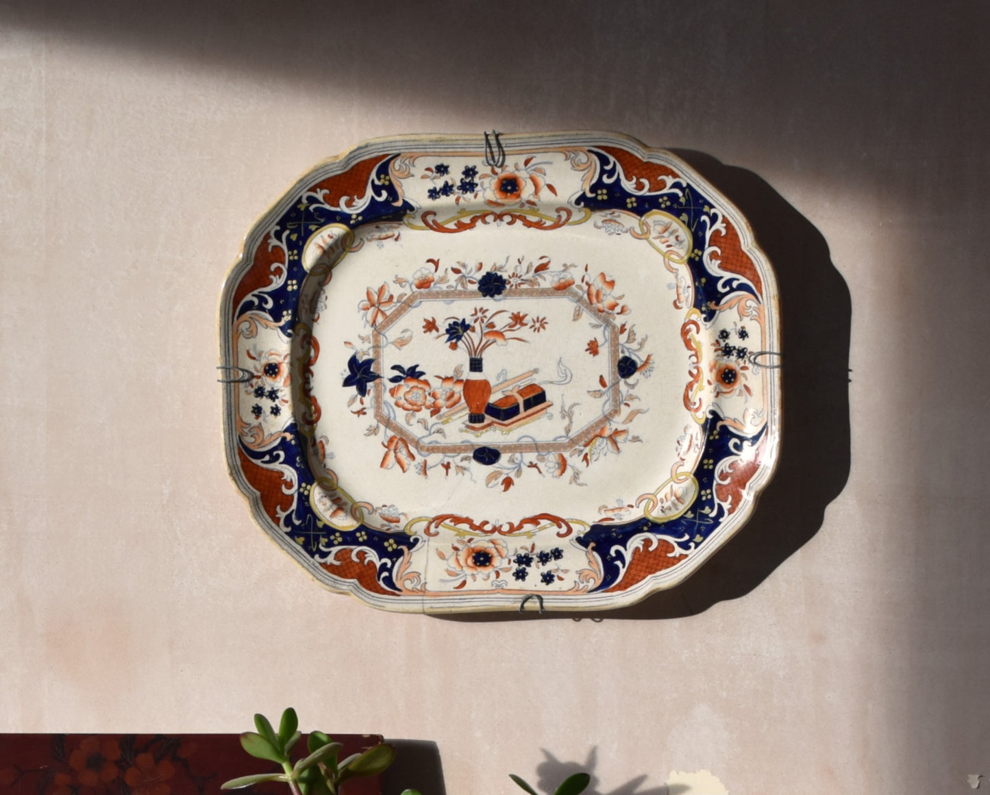 cream, blue and red japanese floral plate hanging on a pink wall