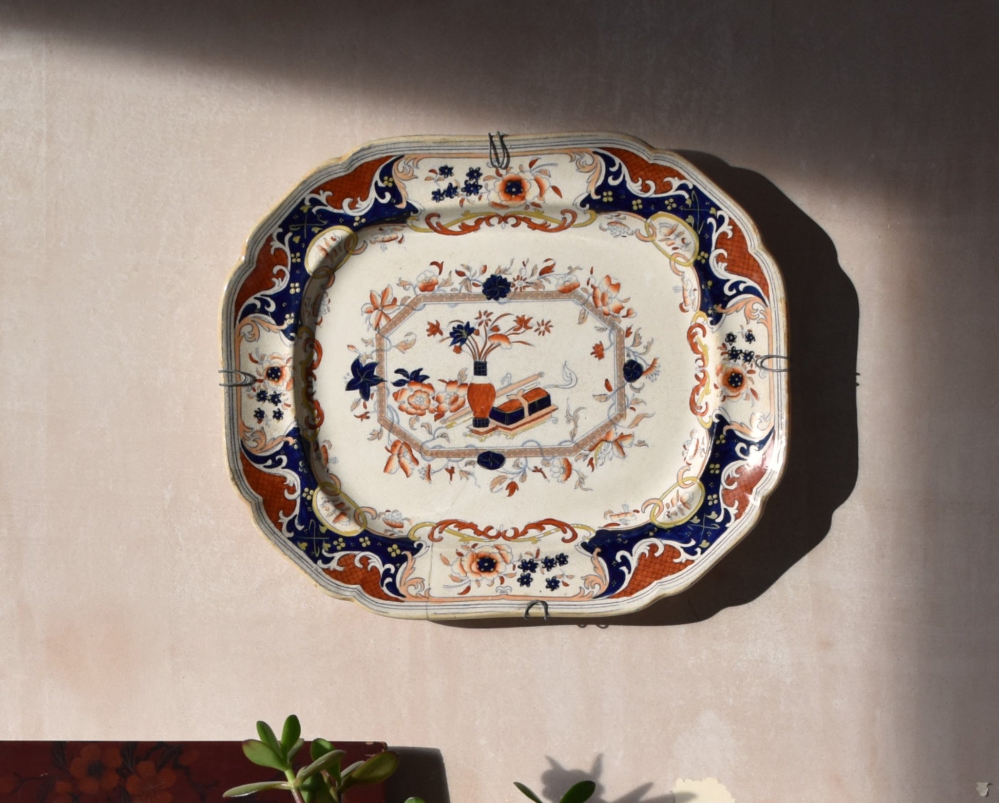 cream, blue and red japanese floral plate hanging on a pink wall
