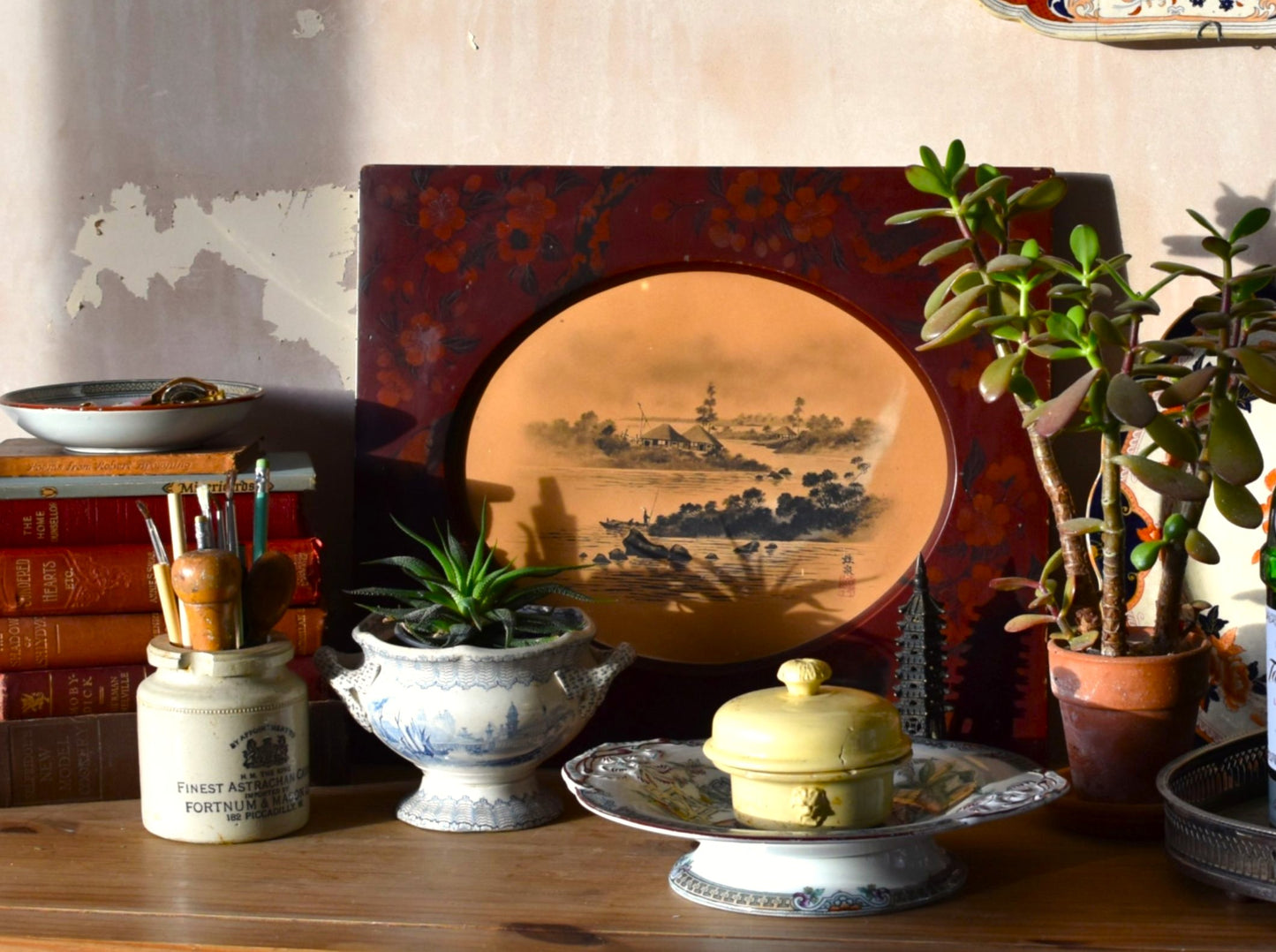 Vintage decor items including a ceramic plate, books, and potted plants on a wooden surface.