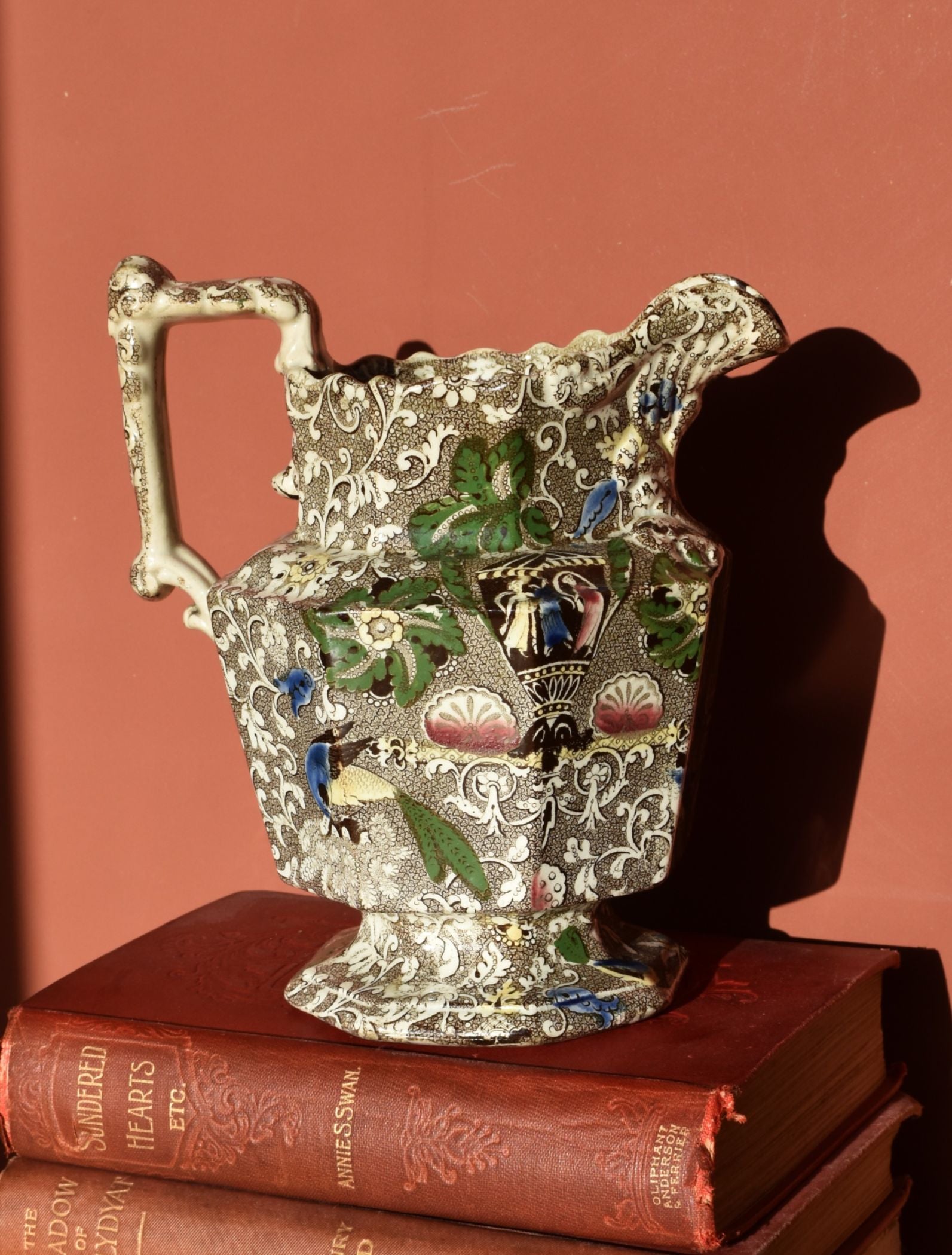 Decorative brown pitcher with colorful engravings on a stack of books against a red background