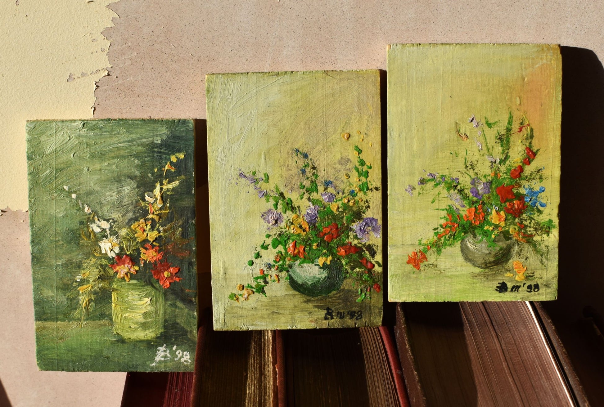 Three small oil paintings of floral arrangements on a textured surface.