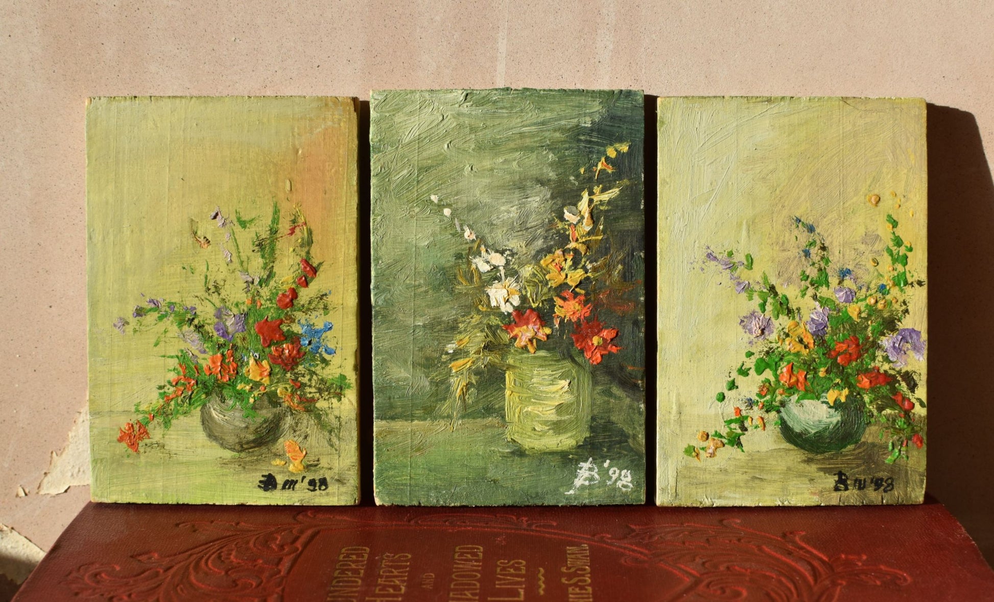 Three panel painting of floral arrangements on a textured surface.