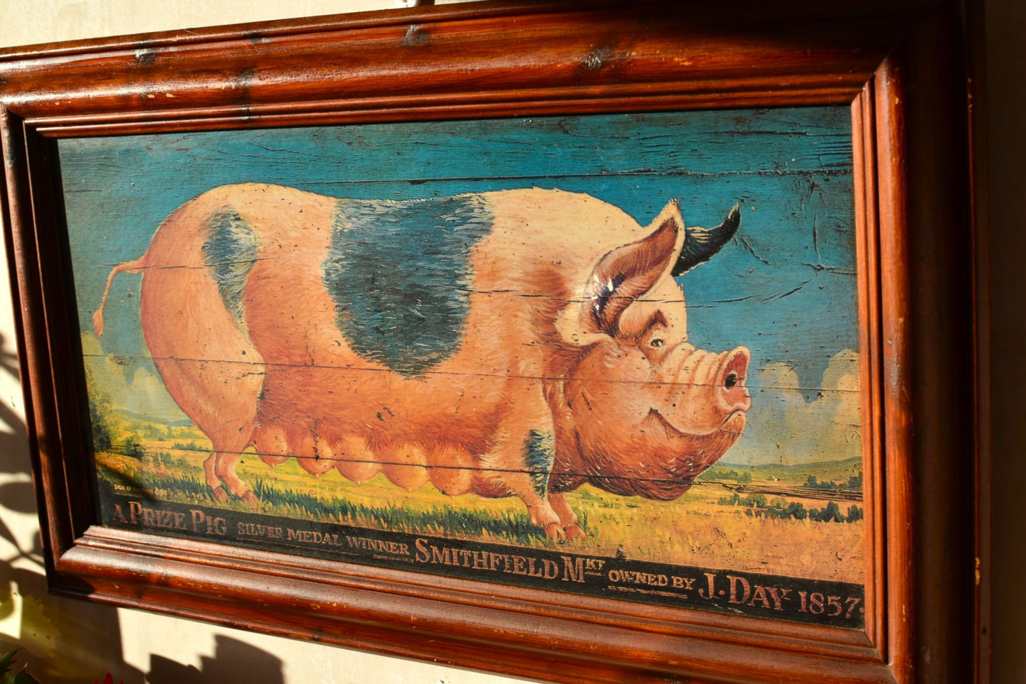 a large painting of a pig in Victorian style with a dark wooden frame hangs on a pink wall