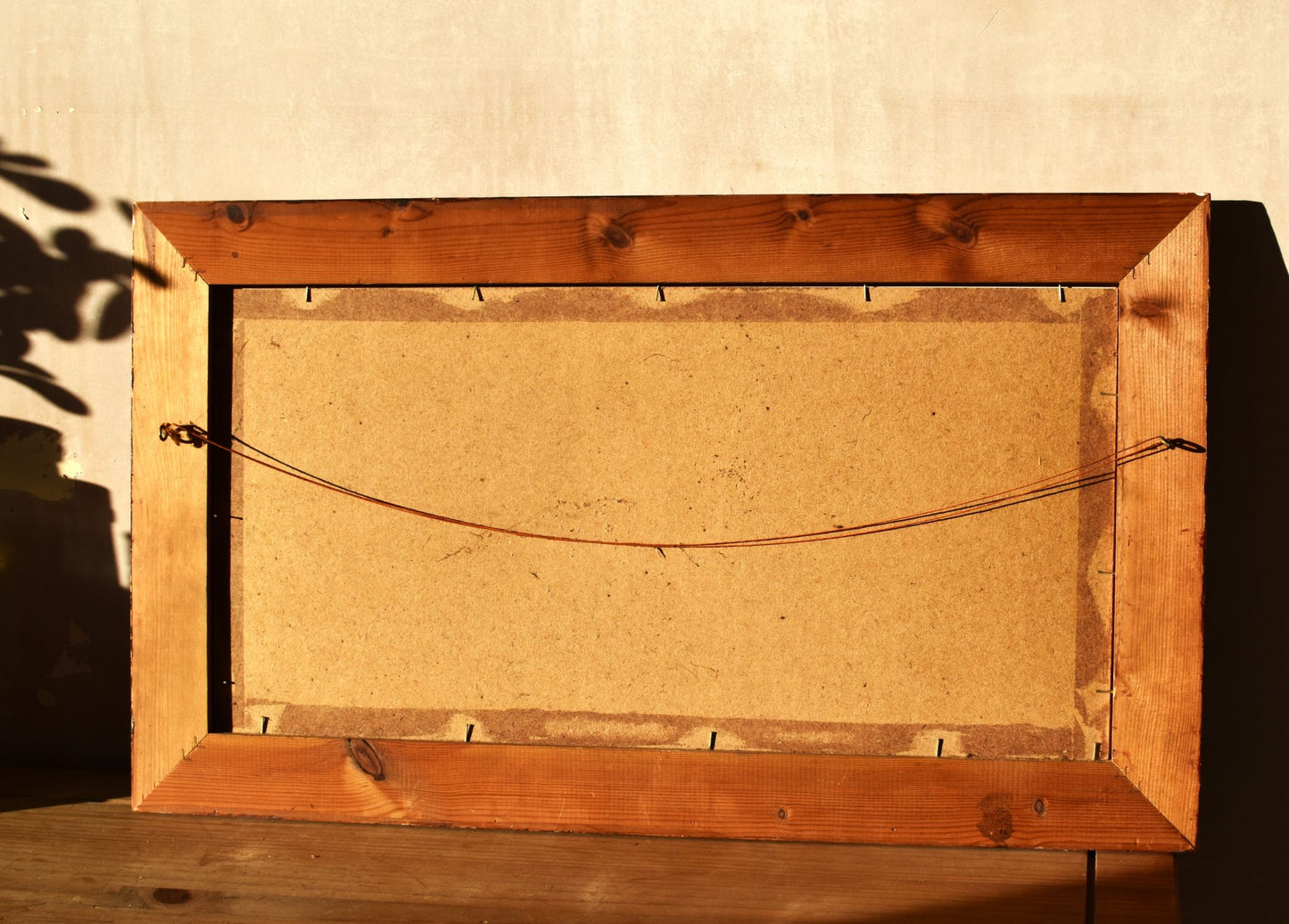 the back of the large frame is made of wooden board, shown against a pale pink wall