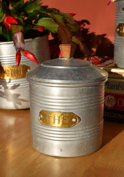 a silver tin with a gold label reading 'The' has a lid with an art deco handle