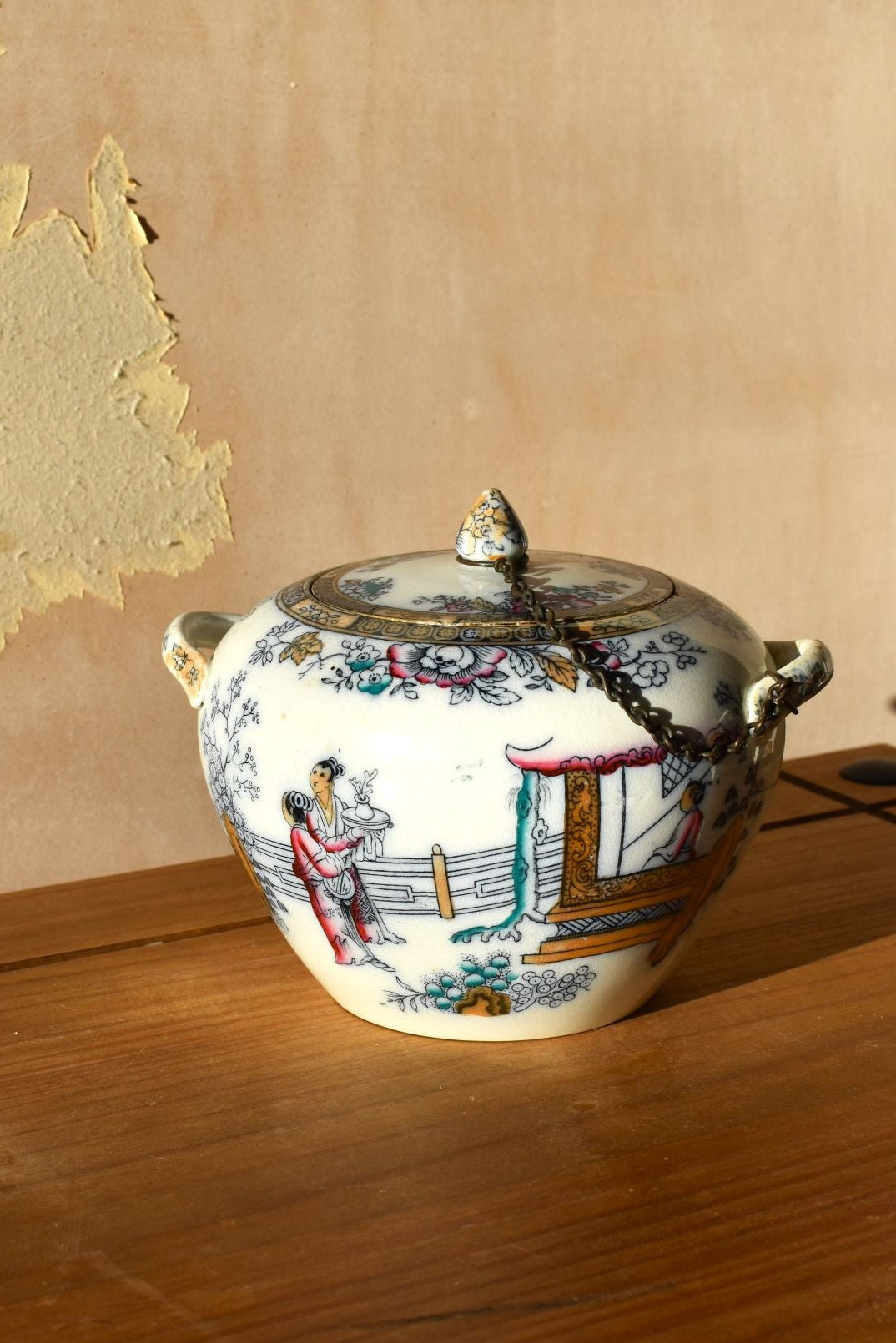 Decorative ceramic tureen with lid on a wooden surface against a beige wall.